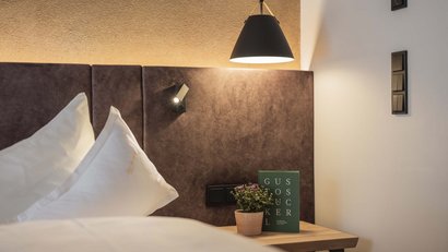 Nachttisch mit Blume und Buch neben Bett mit Kopfteil und Lampe